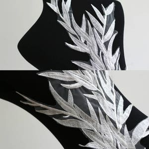 May include: White embroidered lace applique with a delicate leaf design. The lace is on a sheer mesh background.