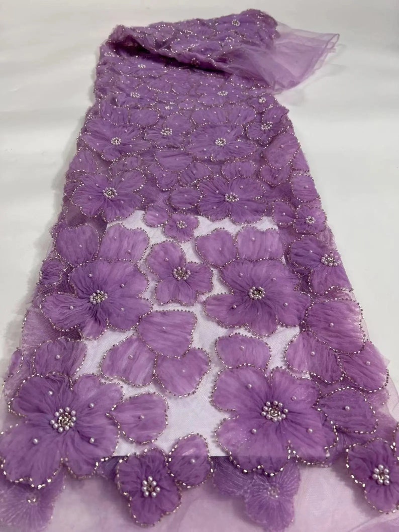 May include: Purple beaded lace fabric with 3D floral appliques. The fabric has a sheer, delicate texture and is adorned with small, pearl-like beads.