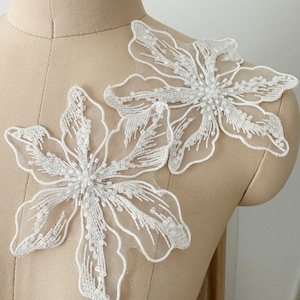 May include: Two white floral appliques with beaded accents. The appliques are made of delicate lace and are perfect for adding a touch of elegance to any project.