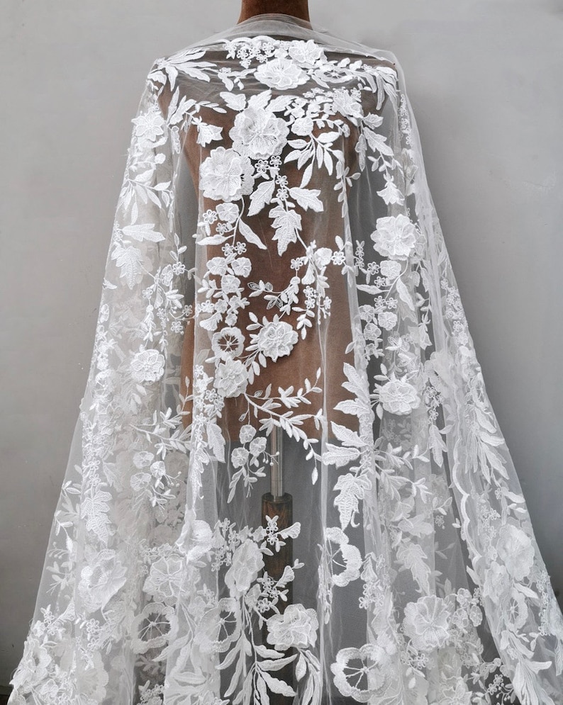 May include: White floral lace fabric with a delicate pattern of flowers and leaves. The lace is sheer and has a soft, romantic feel.
