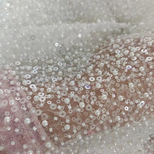 May include: White beaded fabric with a delicate mesh backing. The beads are small and round, creating a shimmering effect.