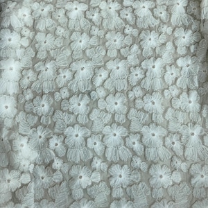 May include: White floral lace fabric with a delicate, 3D flower design. The fabric is sheer and has a soft, flowing texture.