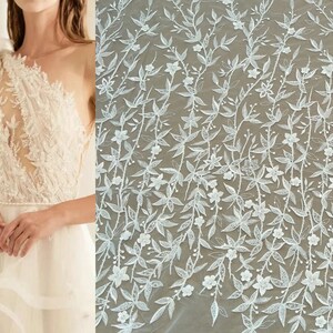 May include: White floral lace fabric with a delicate pattern of leaves and flowers. The lace is sheer and has a soft, romantic feel.