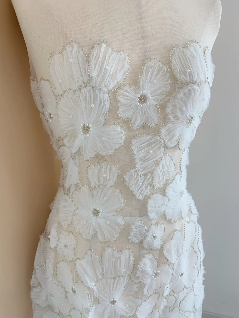 May include: White sheer fabric with 3D floral appliques and pearl embellishments. The fabric is beaded and has a delicate, feminine look.