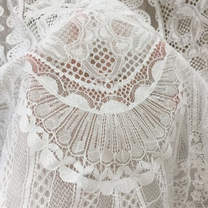 May include: White lace fabric with a delicate floral pattern. The fabric is sheer and has a soft, flowing texture.