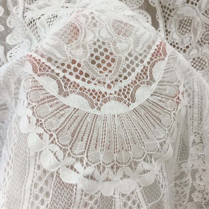 May include: White lace fabric with a delicate floral pattern. The fabric is sheer and has a soft, flowing texture.