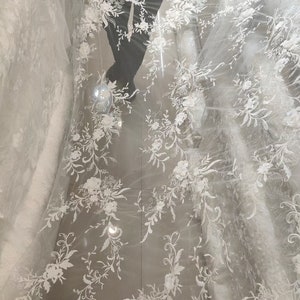 May include: White floral lace fabric with a delicate pattern of flowers and vines. The lace is on a sheer mesh background.