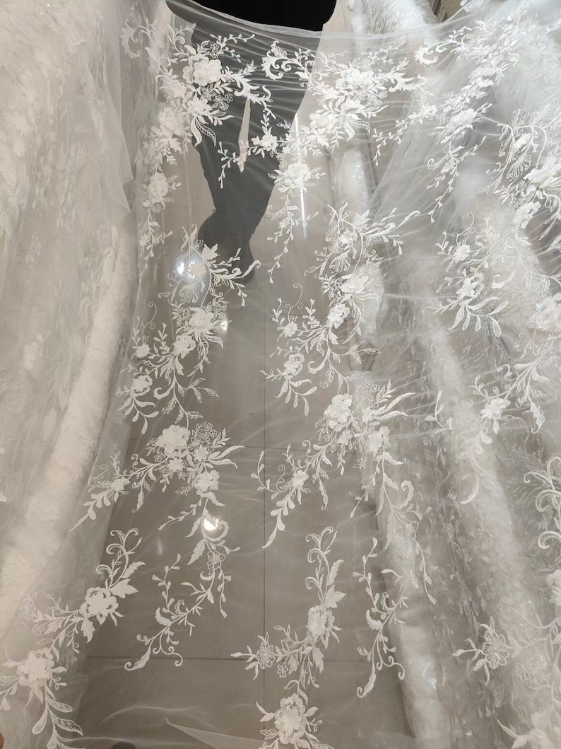 May include: White floral lace fabric with a delicate pattern of flowers and vines. The lace is on a sheer mesh background.