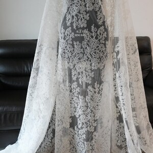 May include: White lace fabric with floral patterns. The delicate lace is draped over a form, showcasing the intricate design. The fabric is semi-transparent, allowing a glimpse of the form beneath. The text "FENG BA" is visible on the form.