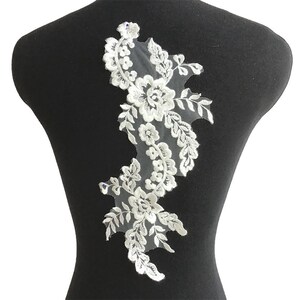 May include: White lace applique with floral designs and delicate leaves. This applique is perfect for adding a touch of elegance to clothing, crafts, or home decor.