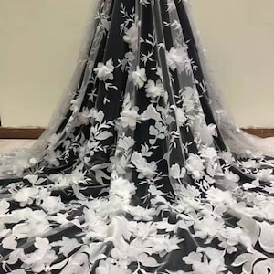 May include: White floral lace fabric with 3D flowers on a black background. The lace is delicate and intricate, with a soft, flowing texture. The flowers are large and prominent, adding a touch of elegance and sophistication to the fabric.