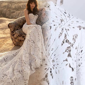 May include: White lace fabric with a floral pattern. The fabric is delicate and intricate, with a soft, flowing texture. It is perfect for creating elegant and romantic garments.