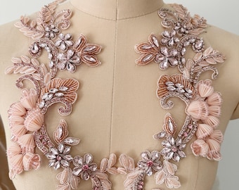 Könnte beinhalten: Ein Paar zarte florale Applikationen mit rosa und beigefarbenen Stoffblumen, Strasssteinen und Perlen. Die Applikationen sind perfekt, um Brautkleidern, Brautkleidern oder anderen Kleidungsstücken für besondere Anlässe einen Hauch von Eleganz zu verleihen.