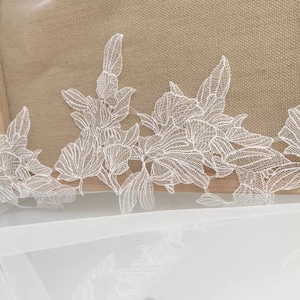 May include: White lace trim featuring a floral design. The lace is delicate and intricate, with a variety of flower shapes and sizes.