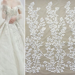 May include: White floral lace fabric with a delicate vine pattern. The lace is made of small, white leaves that are sewn onto a sheer mesh background.