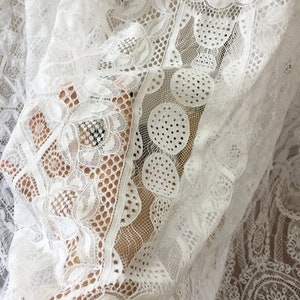 May include: White lace fabric with a delicate floral pattern. The fabric is sheer and has a soft, flowing texture.