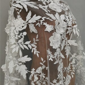 May include: White floral lace fabric with a delicate pattern of flowers and leaves. The lace is on a sheer mesh background.