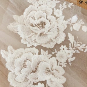 Puede incluir: Bordado floral blanco sobre una tela beige transparente. El bordado presenta flores grandes y peque&ntilde;as con detalles intrincados.