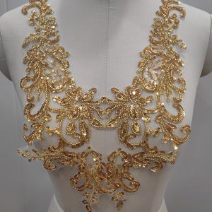May include: Gold sequined lace applique with a floral design. The applique is on a white background and is perfect for adding a touch of sparkle to any project.