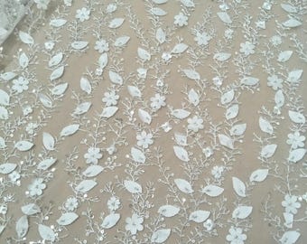 May include: White floral lace fabric with sequins and 3D flowers. The fabric has a delicate, intricate design with small leaves and flowers.