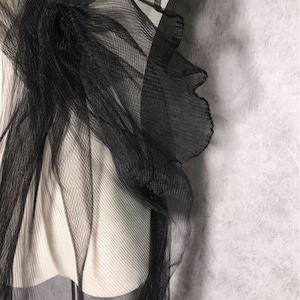 May include: Black sheer fabric with a ruffled edge. The fabric is draped over a white mannequin.