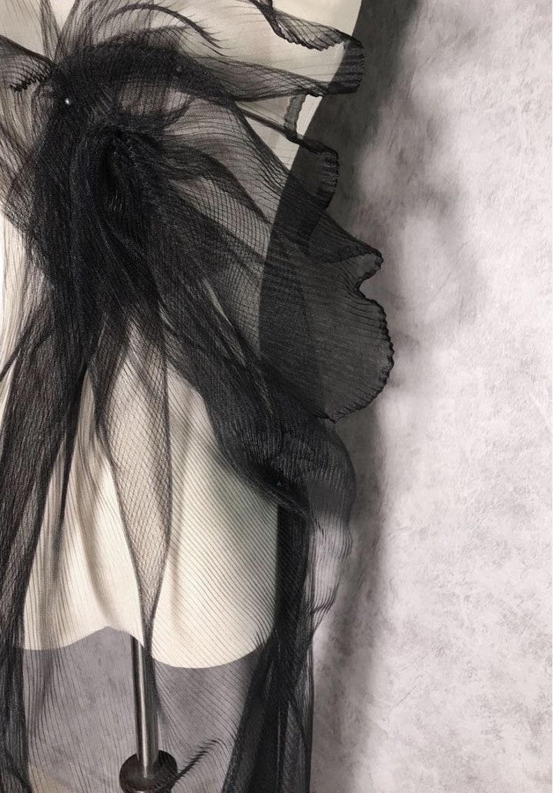 May include: Black sheer fabric with a ruffled edge. The fabric is draped over a white mannequin.
