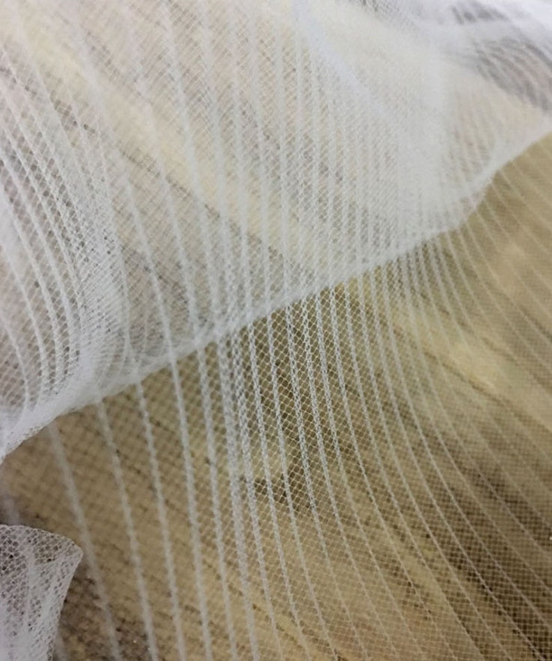 May include: White tulle fabric with a striped pattern. The fabric is soft and delicate, and it has a slightly shimmery finish.