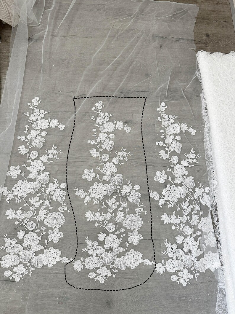 May include: White floral lace fabric with a delicate floral pattern. The lace is arranged in three sections, with the center section being slightly larger than the two side sections. The lace is laid out on a light gray surface.