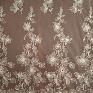May include: White floral embroidery on a sheer ivory fabric. The fabric has a delicate, intricate design with small flowers and leaves.