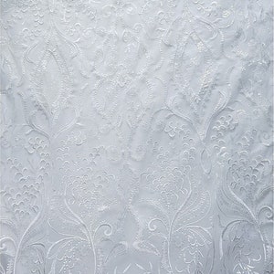 May include: White embroidered fabric with a floral pattern. The fabric has a delicate, intricate design with small, white flowers and leaves.