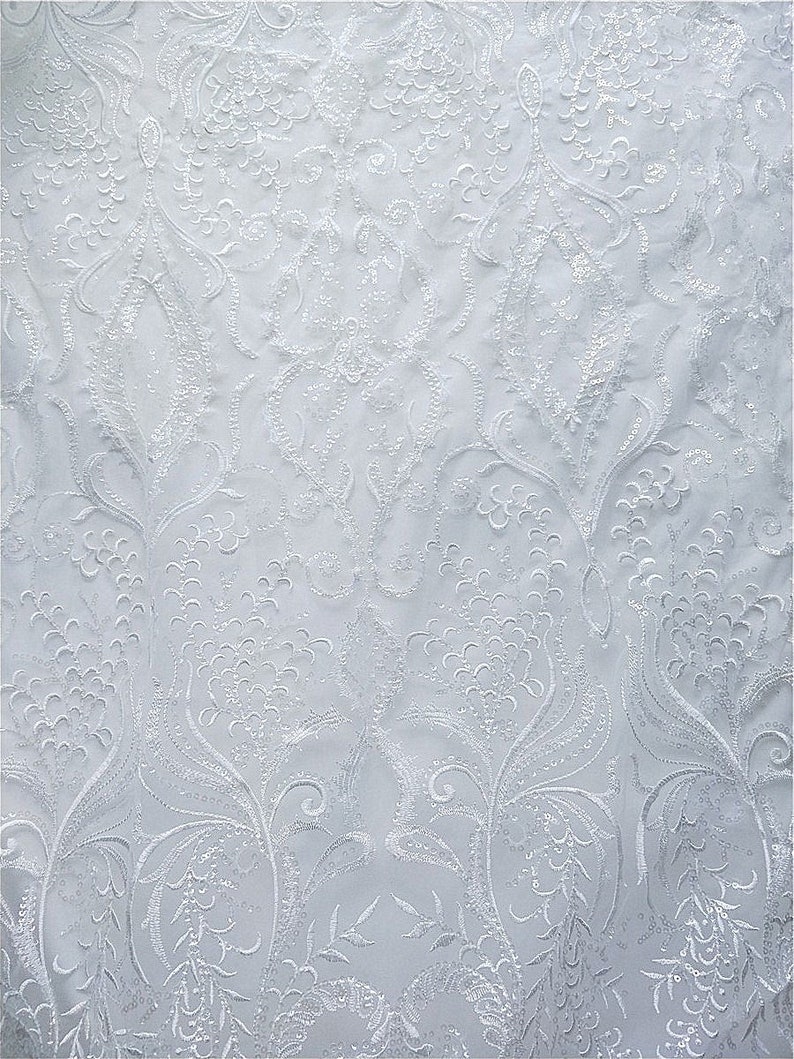 May include: White embroidered fabric with a floral pattern. The fabric has a delicate, intricate design with small, white flowers and leaves.