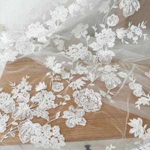 May include: White floral lace fabric with sequins on a sheer mesh background.