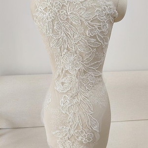 May include: White beaded floral applique with a delicate lace design. The applique is perfect for adding a touch of elegance to any garment.