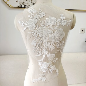 May include: White floral lace applique with delicate embroidery details. This intricate design is perfect for adding a touch of elegance to wedding dresses, bridal accessories, or other craft projects.