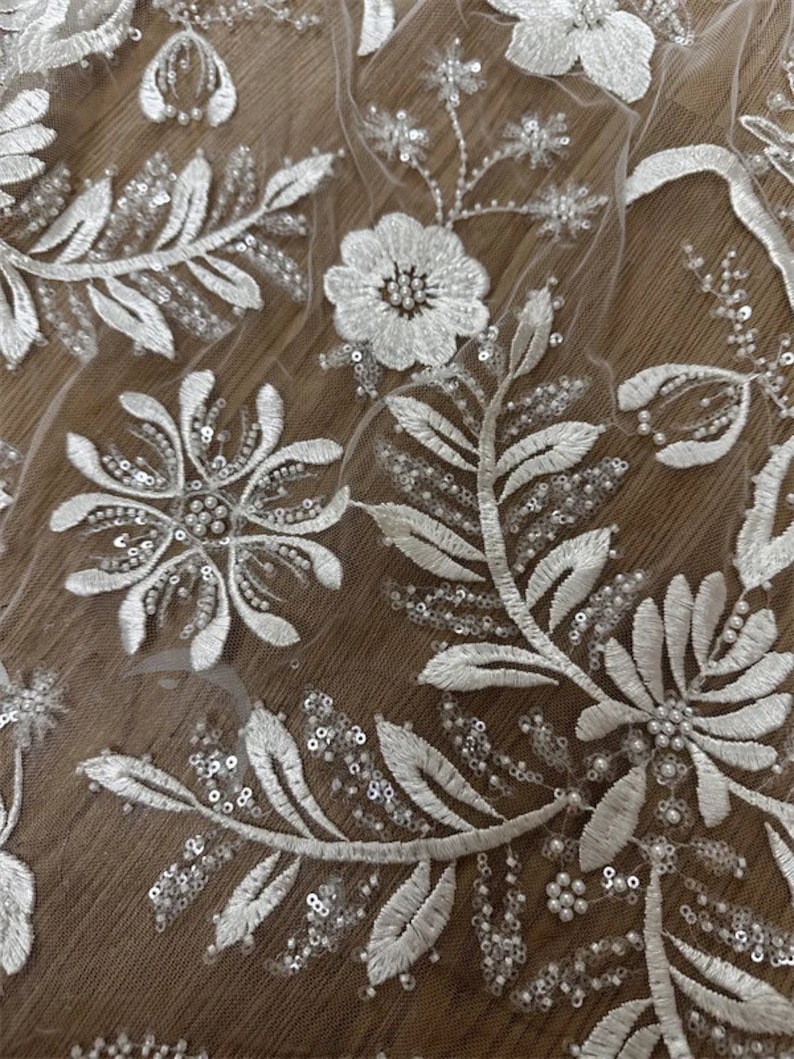 May include: White floral lace fabric with pearl and sequin embellishments.