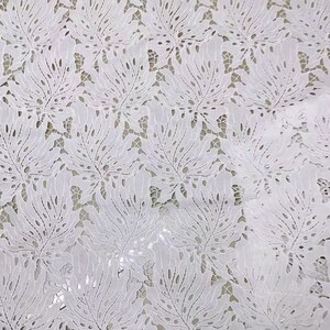 May include: White lace fabric with a delicate floral pattern. The fabric has a cut-out design that creates a see-through effect.
