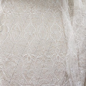 May include: White lace fabric with a delicate floral pattern. The lace is sheer and has a soft, flowing texture.