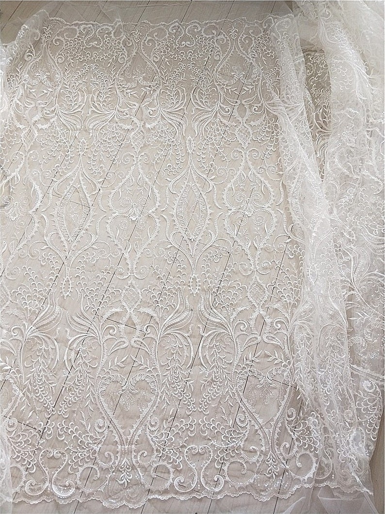 May include: White lace fabric with a delicate floral pattern. The lace is sheer and has a soft, flowing texture.