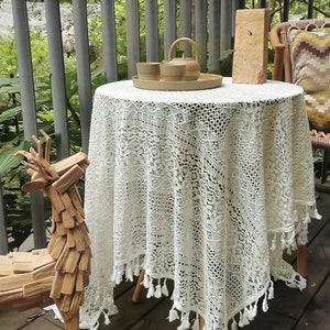 Puede incluir: Mantel de mesa de crochet blanco con ribete de flecos, una escultura de ciervo de madera y una mesa pequeña con una tetera y tazas en una bandeja.