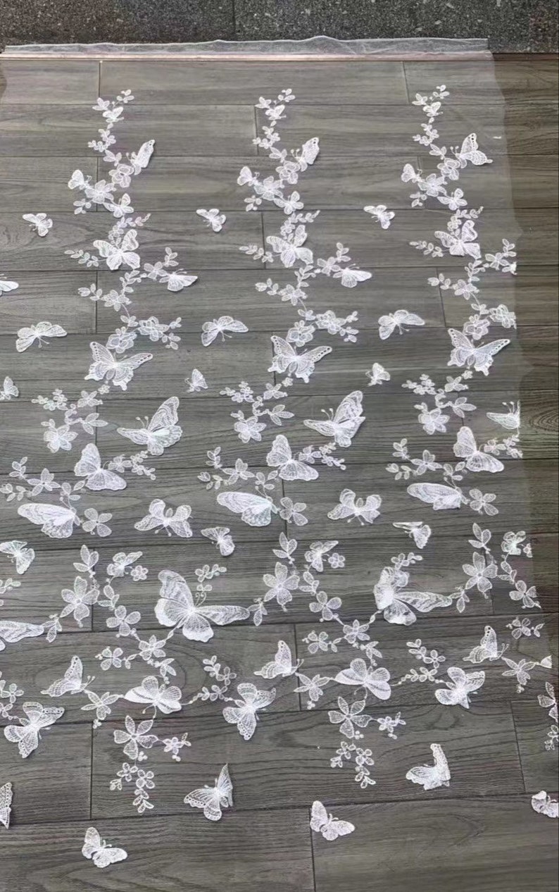 Pu&ograve; includere: Tessuto di pizzo bianco con un delicato motivo a farfalla. Le farfalle sono ricamate su uno sfondo di rete trasparente.