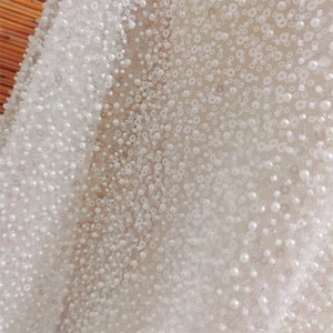 May include: White beaded fabric with a delicate, sheer texture. The fabric is covered in small, white beads that are evenly spaced.