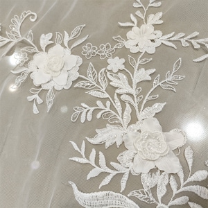 May include: White floral lace fabric with 3D flowers and sequins. The fabric has a delicate and intricate design with a sheer background.