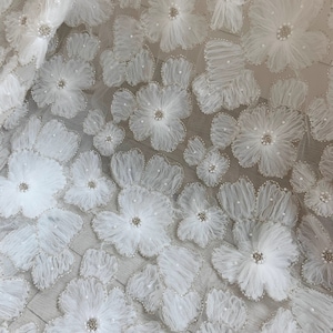 May include: White floral lace fabric with 3D flowers and pearl embellishments. The fabric has a delicate and intricate design.