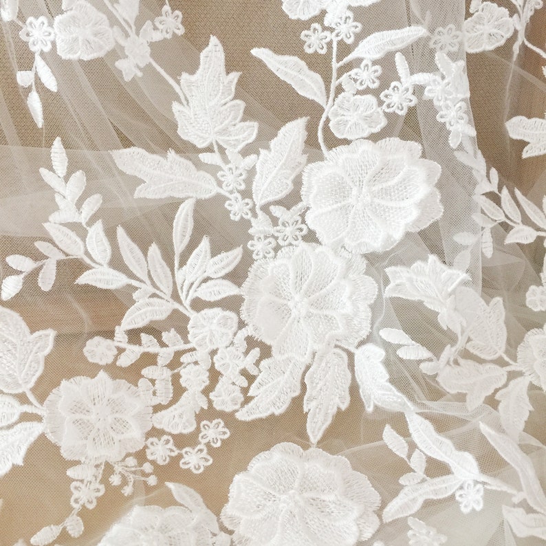 May include: White floral lace fabric with a delicate pattern of flowers and leaves. The lace is on a sheer, white background.