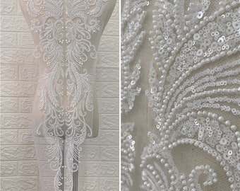 Op de afbeelding: Witte, met kralen en pailletten bezette kant-applicatie met een bloemenmotief. De applicatie is op een transparant gaasstof en is perfect om een ​​toets van elegantie toe te voegen aan elk kledingstuk.