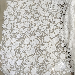 May include: White floral lace fabric with a delicate pattern of flowers and leaves. The lace is sheer and has a soft, flowing texture.