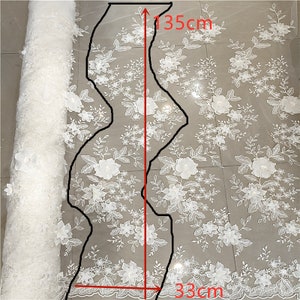 May include: White floral lace fabric with a 3D flower design. The fabric is 135cm long and 33cm wide. The fabric is shown rolled up and unrolled.