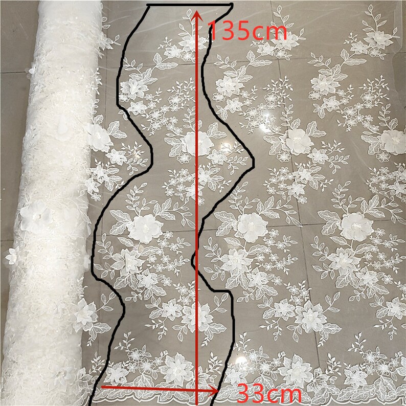 May include: White floral lace fabric with a 3D flower design. The fabric is 135cm long and 33cm wide. The fabric is shown rolled up and unrolled.