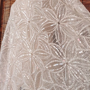 Peut inclure: Tissu blanc avec un motif d&eacute;licat de petites paillettes iris&eacute;es dispos&eacute;es en forme de fleur.