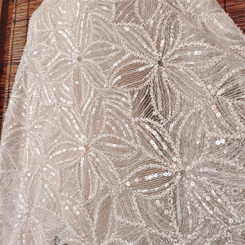 Peut inclure: Tissu blanc avec un motif d&eacute;licat de petites paillettes iris&eacute;es dispos&eacute;es en forme de fleur.